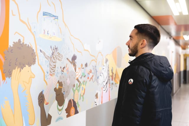 Un membre de l'association devant une fresque murale, dans un couloir de l'hôpital
